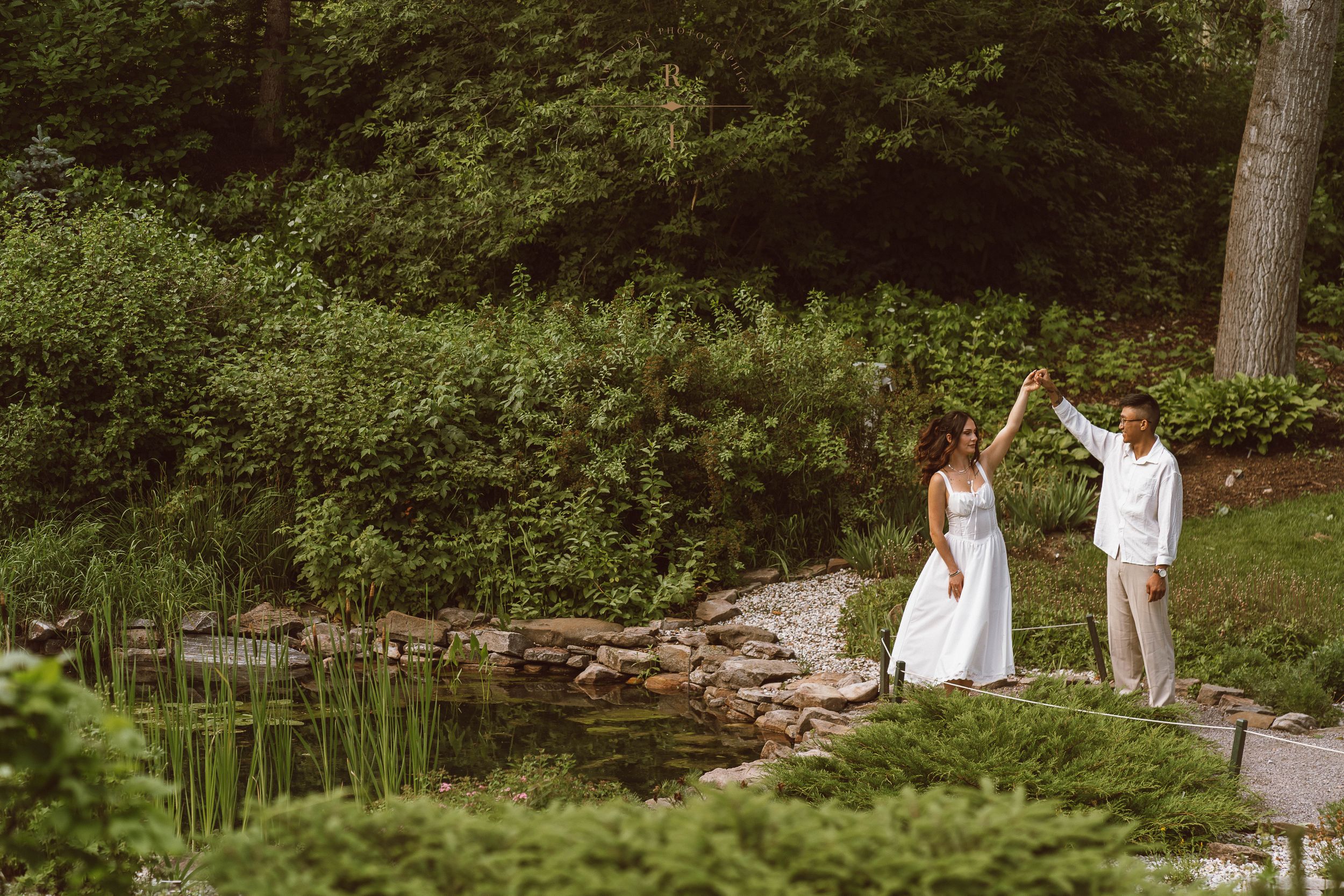 Bride and groom celebrate outdoors near a serene garden pond surrounded by lush greenery on their wedding day.