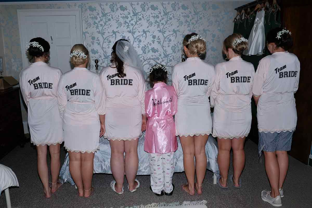Bridal party in matching Team Bride robes standing together, with bride in veil in the bridal suite at Blaithwaite House