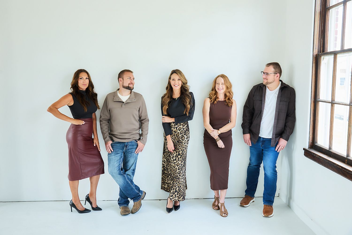Five professionally dressed adults smiling and posing together against a white wall in a modern studio setting.