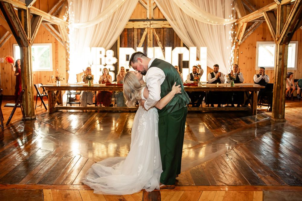 Bride and groom share first dance in rustic barn wedding venue with wooden floors and elegant draped fabric decor.