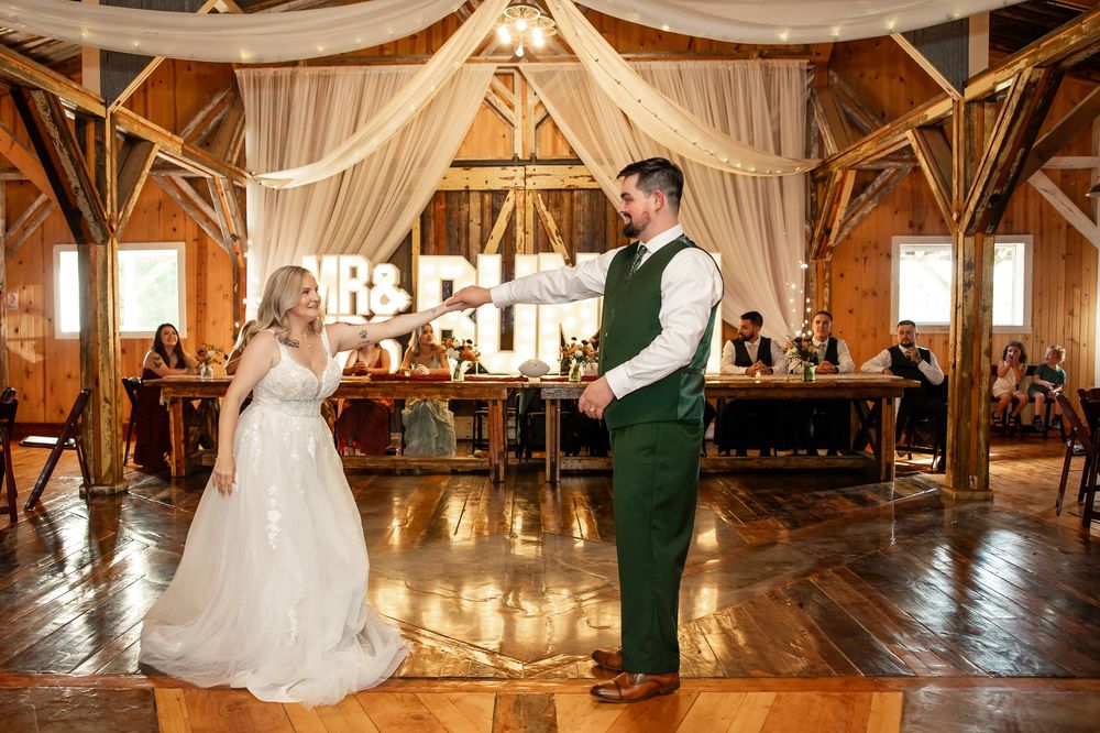 Bride and groom share first dance in a rustic barn wedding venue decorated with white draping and warm string lights.
