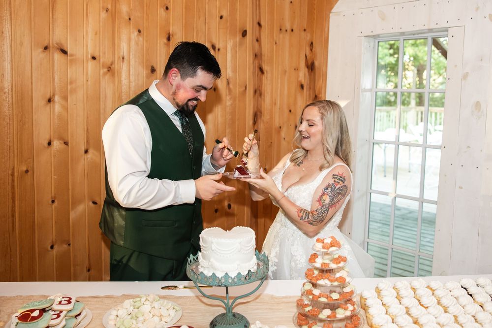 Bride and groom cutting their wedding cake together at a rustic wooden venue with cupcake tower nearby.