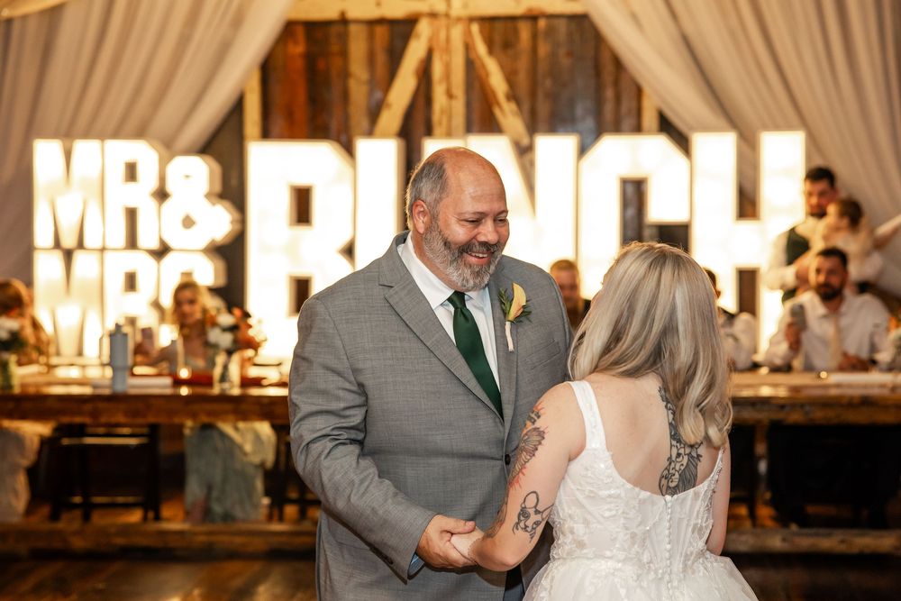 Bride and groom share first dance at wedding reception with Mr. & Mrs. marquee sign glowing in background.