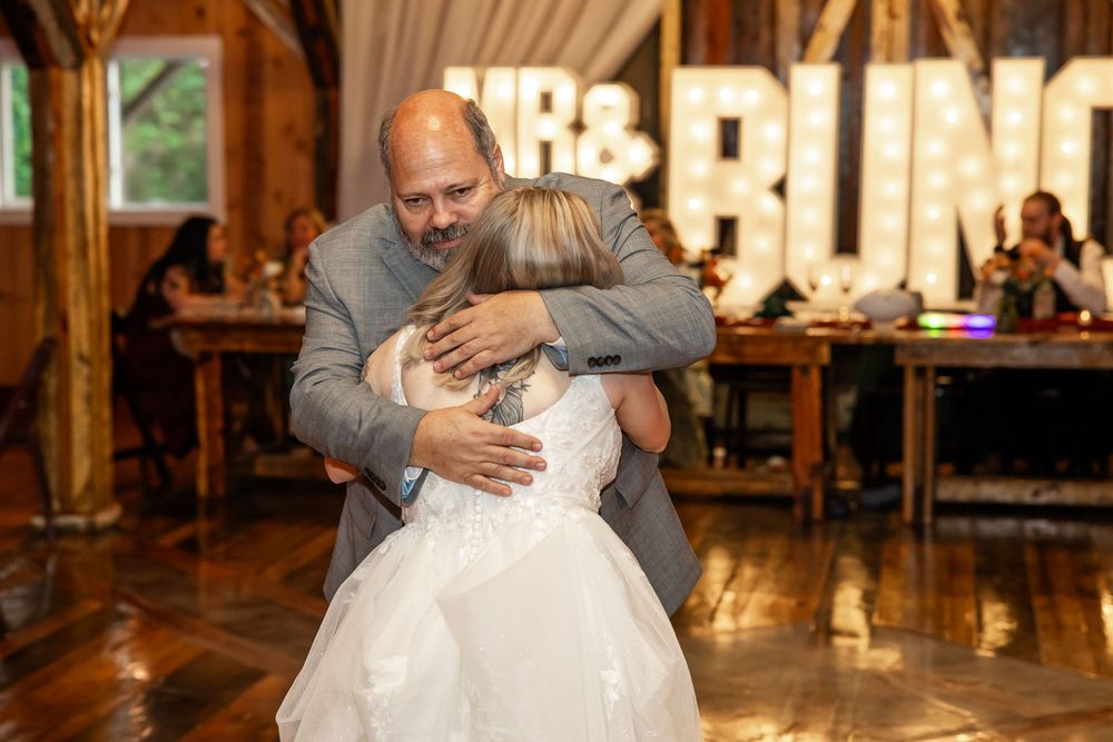 Father and bride share an emotional hug during father-daughter dance at rustic barn wedding reception.