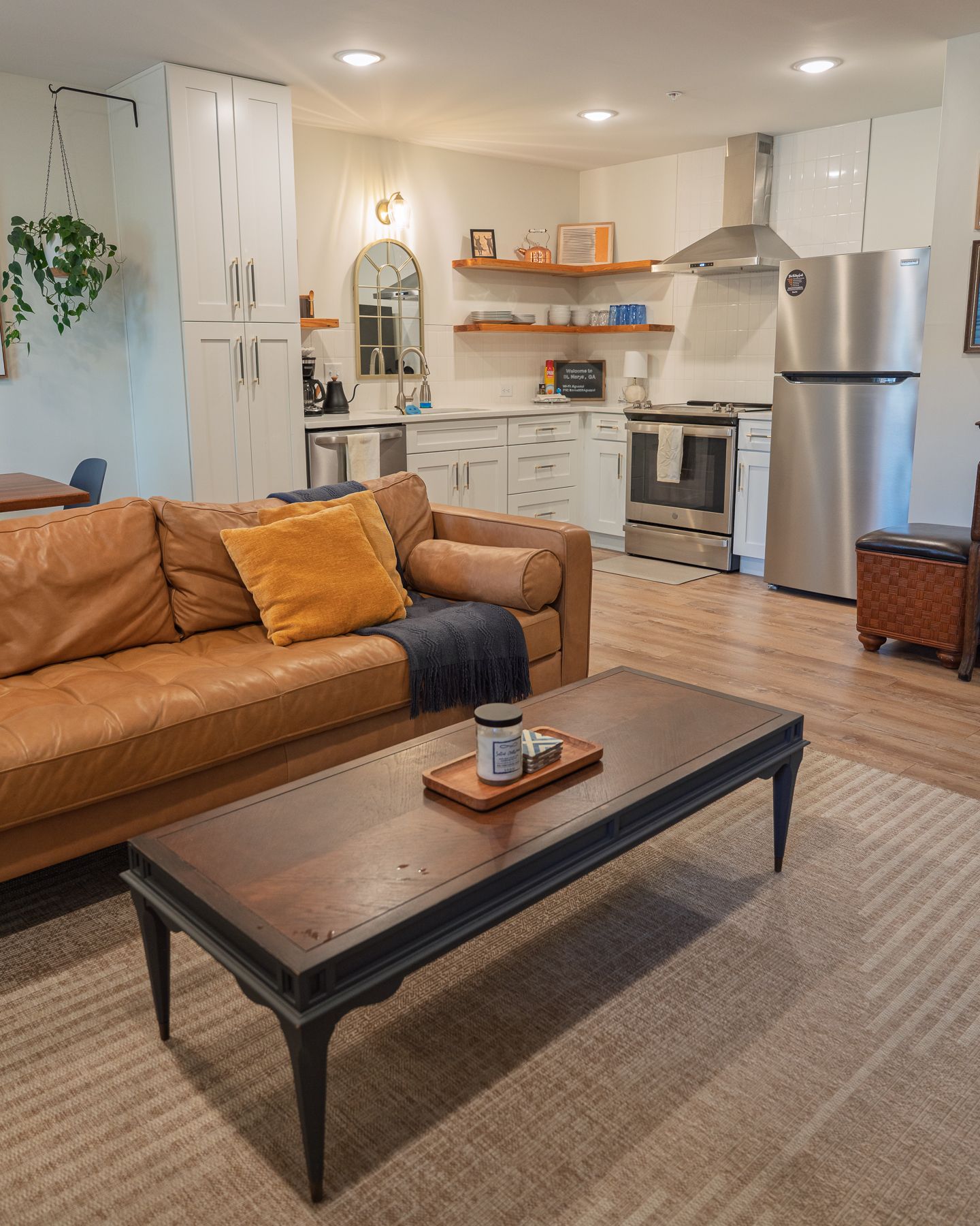 Modern open living room with tan leather sofa, wooden coffee table, and stainless steel kitchen appliances in background, St. Mary's GA.
