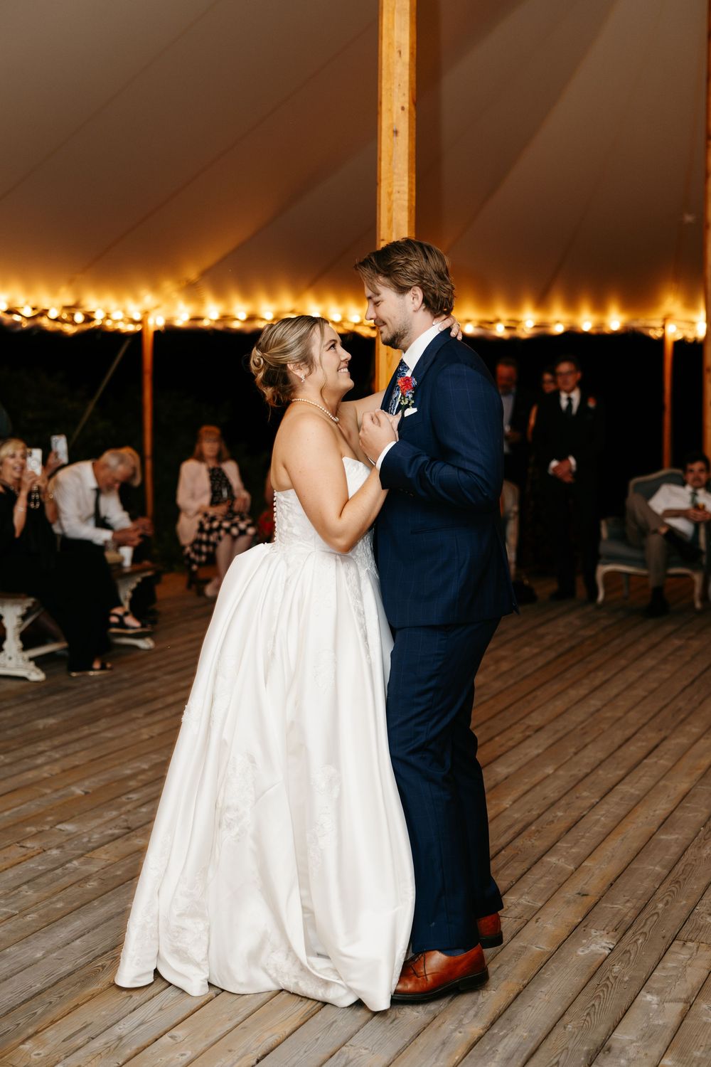 Bride and groom share their first dance under a warmly lit tent at an elegant outdoor wedding reception.