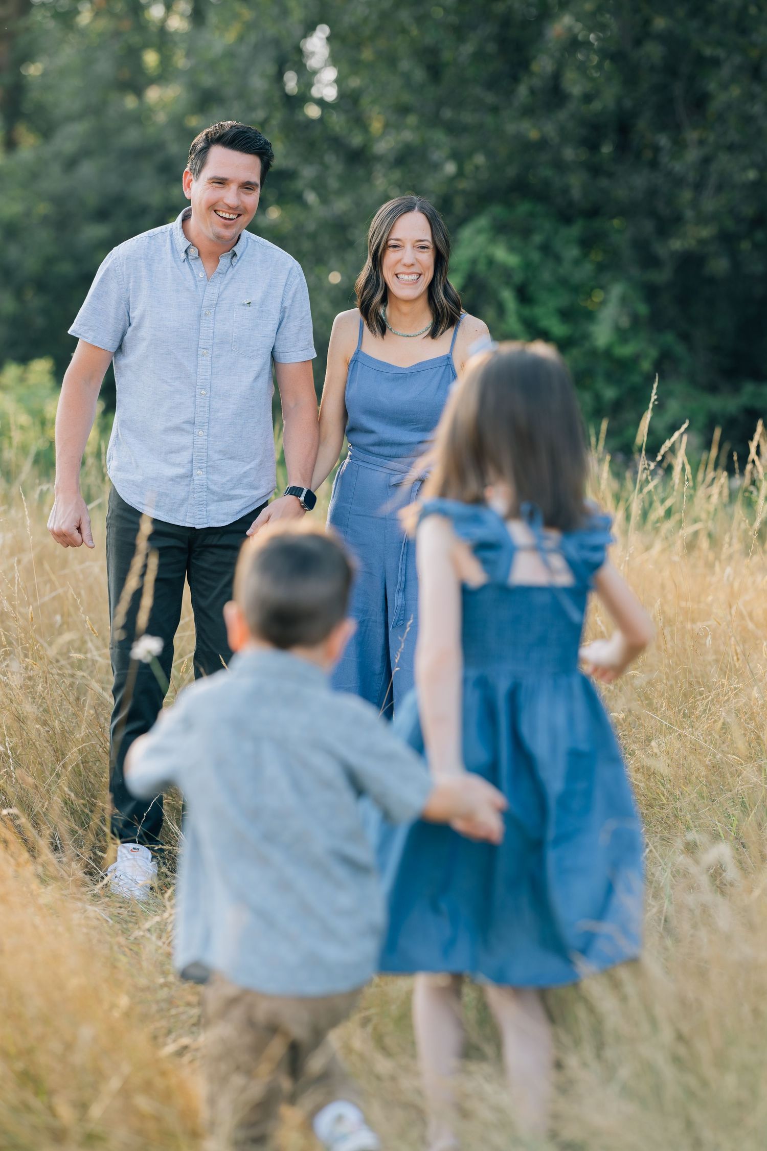 A joyful family of four walks through a golden field, with two children running toward their smiling parents on a sunny day.