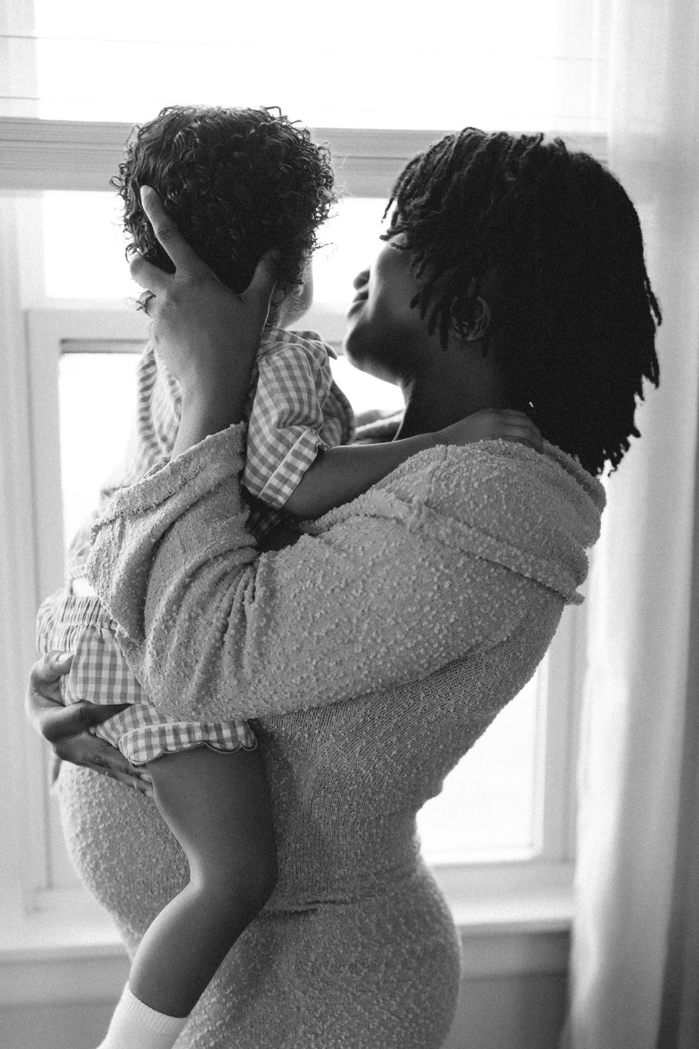 Black and white photo of a pregnant mother tenderly holding and gazing at her young child.