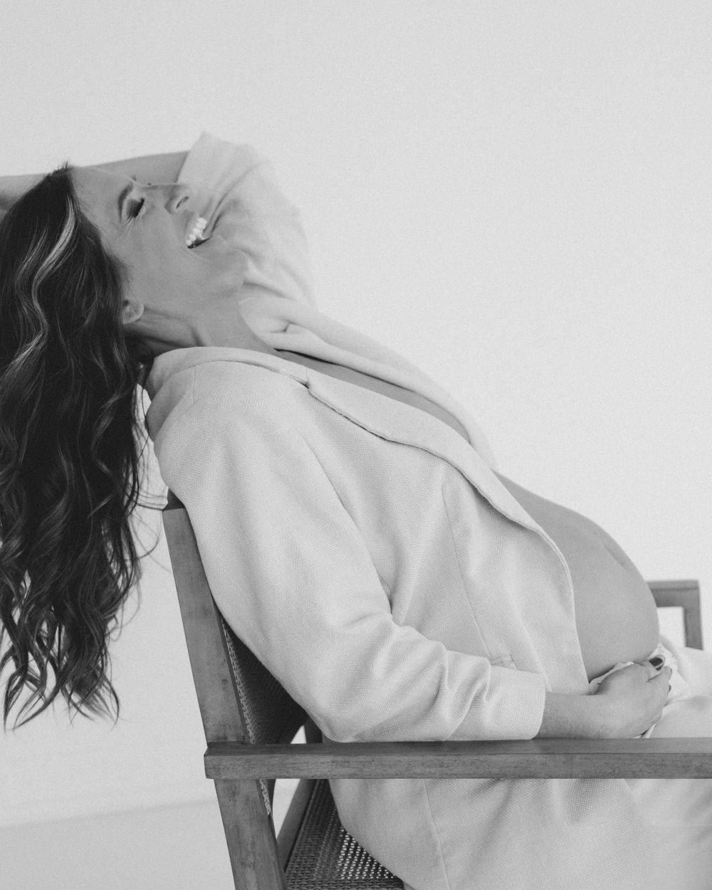 Black and white photo of pregnant woman relaxing in chair wearing cozy hoodie.