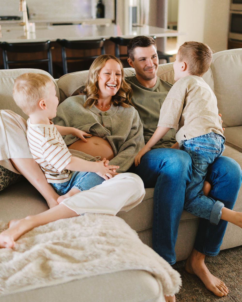 Happy family with two young boys laughing together on a couch during maternity photo session.