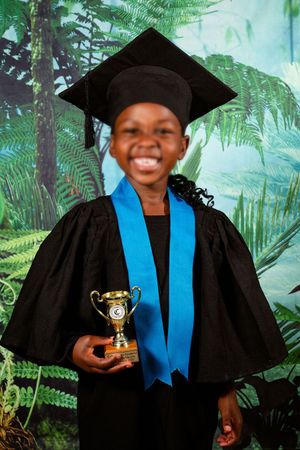 An image of school boy smiling at the camera for their Grade R graduation portrait, holding their graduation trophy.