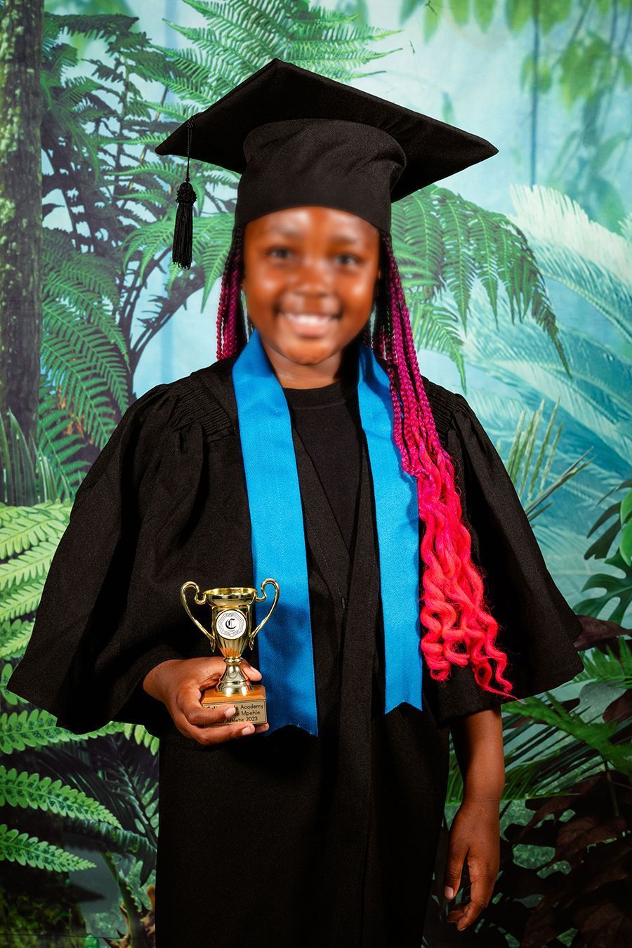 An picture of  preschool girl smiling at the camera for their Grade R graduation portrait, holding their graduation trophy.