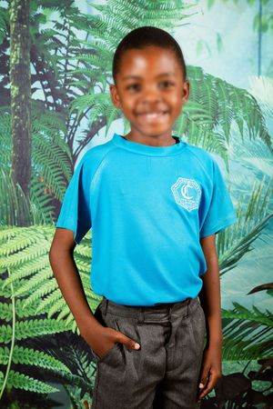 A picture of a child smiling at the camera, wearing their blue school t shirt.