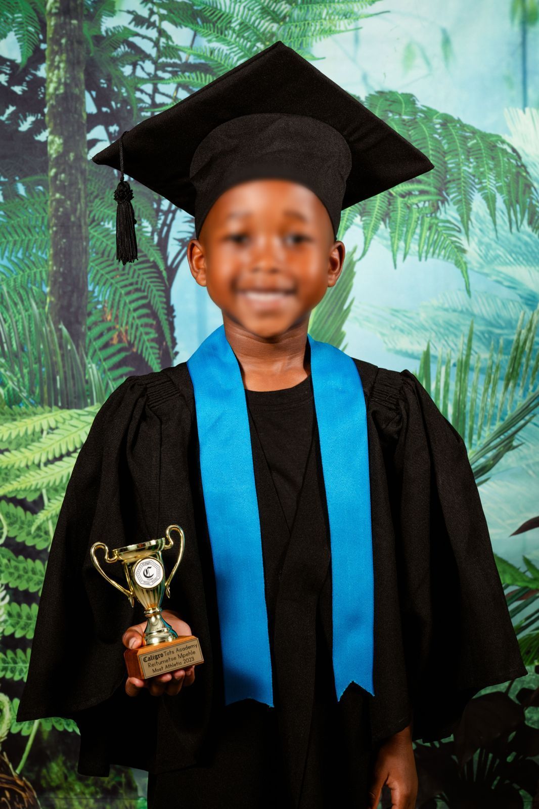An picture of  preschooler smiling at the camera for their Grade R graduation portrait, holding their graduation trophy.