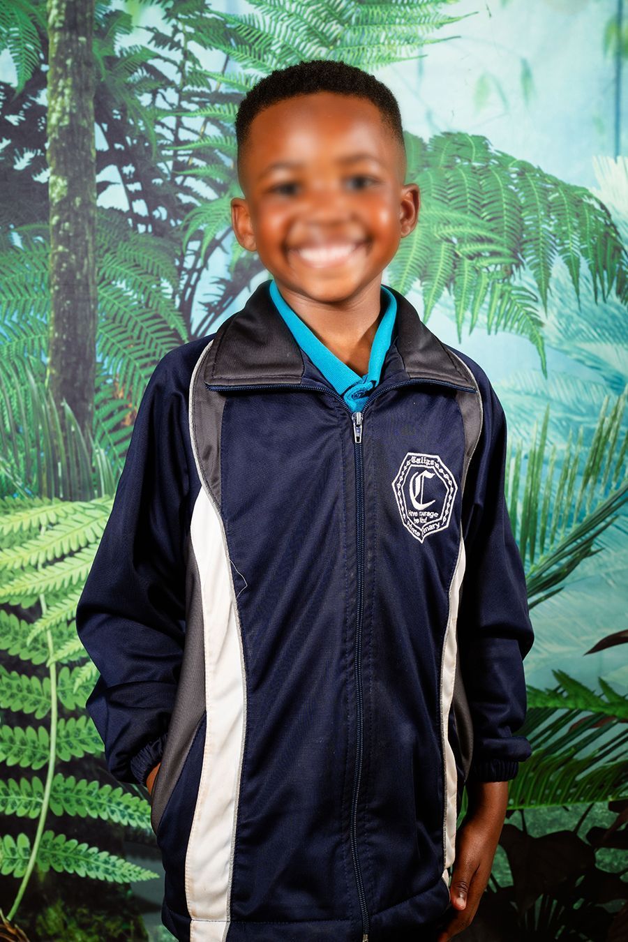 An image of a preschooler, wearing their school uniform, smiling for their picture day.