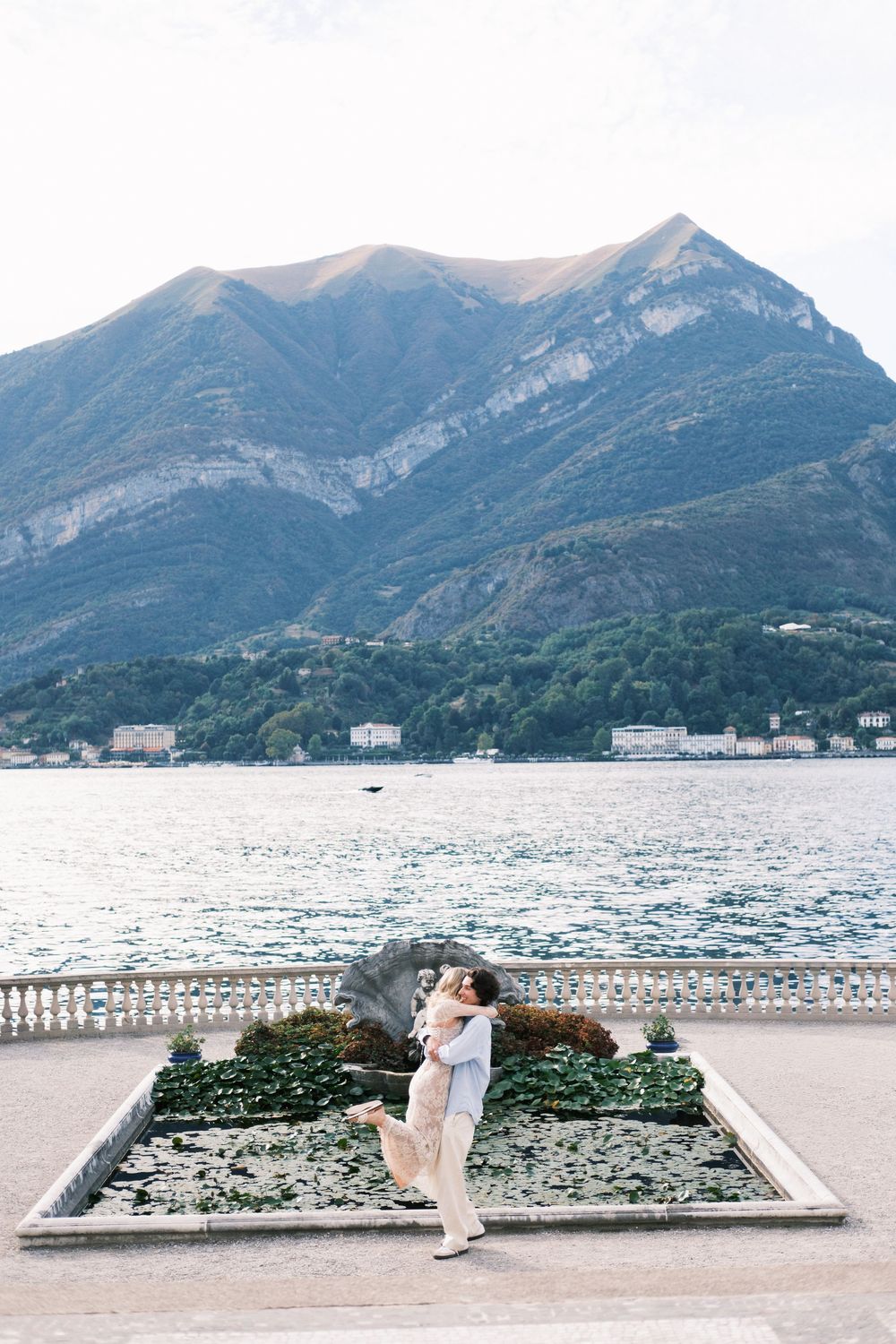 Couple embracing on elegant lakeside terrace with stunning mountain backdrop at Lake Como, Italy.