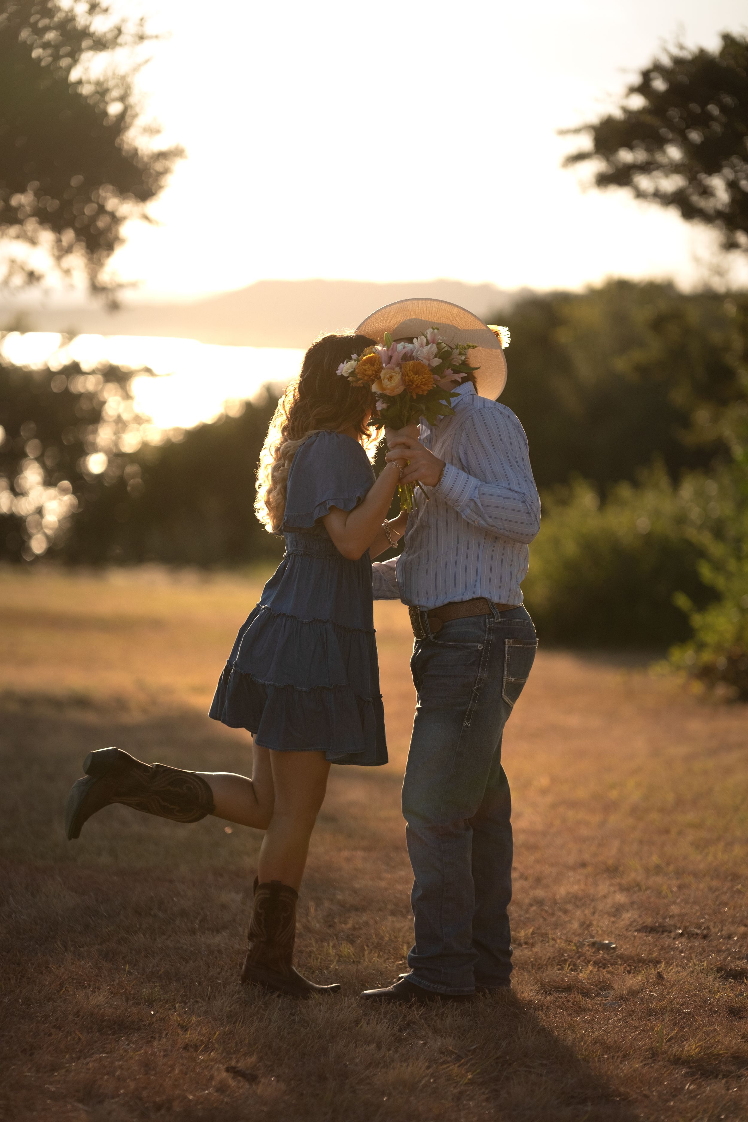 Couple sharing a kiss hidden behind wildflower bouquet at sunset in a rustic outdoor field in Belton Texas