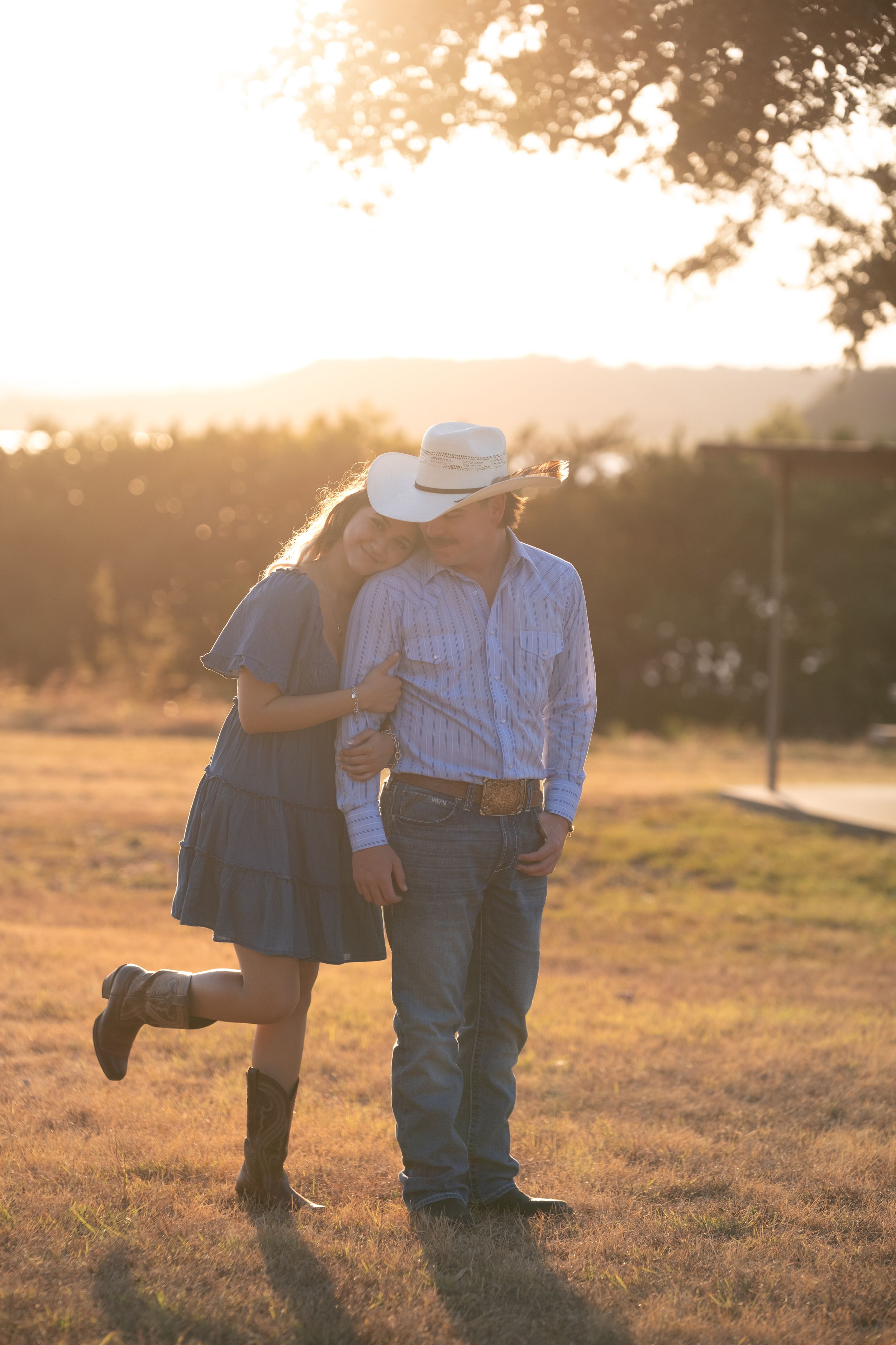 Couple walking hand in hand at sunset, man in cowboy hat and woman in blue dress with boots in Belton Texas