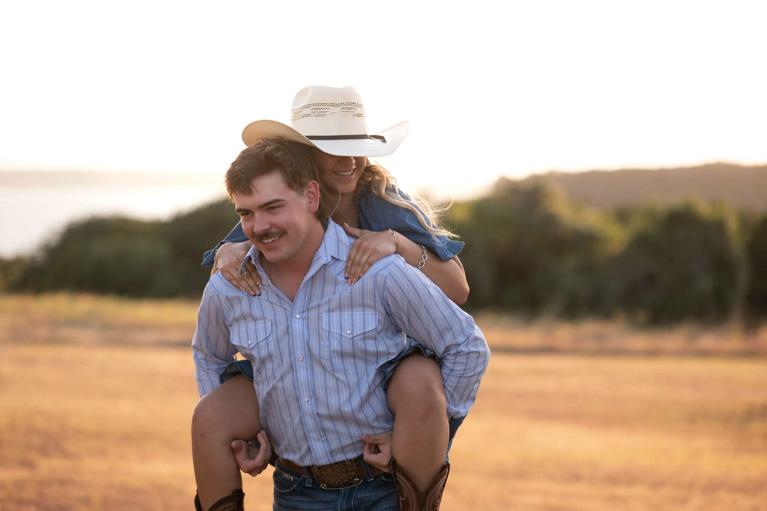 Smiling man giving woman a piggyback ride in a golden sunset field, both in casual country attire in Belton Texas