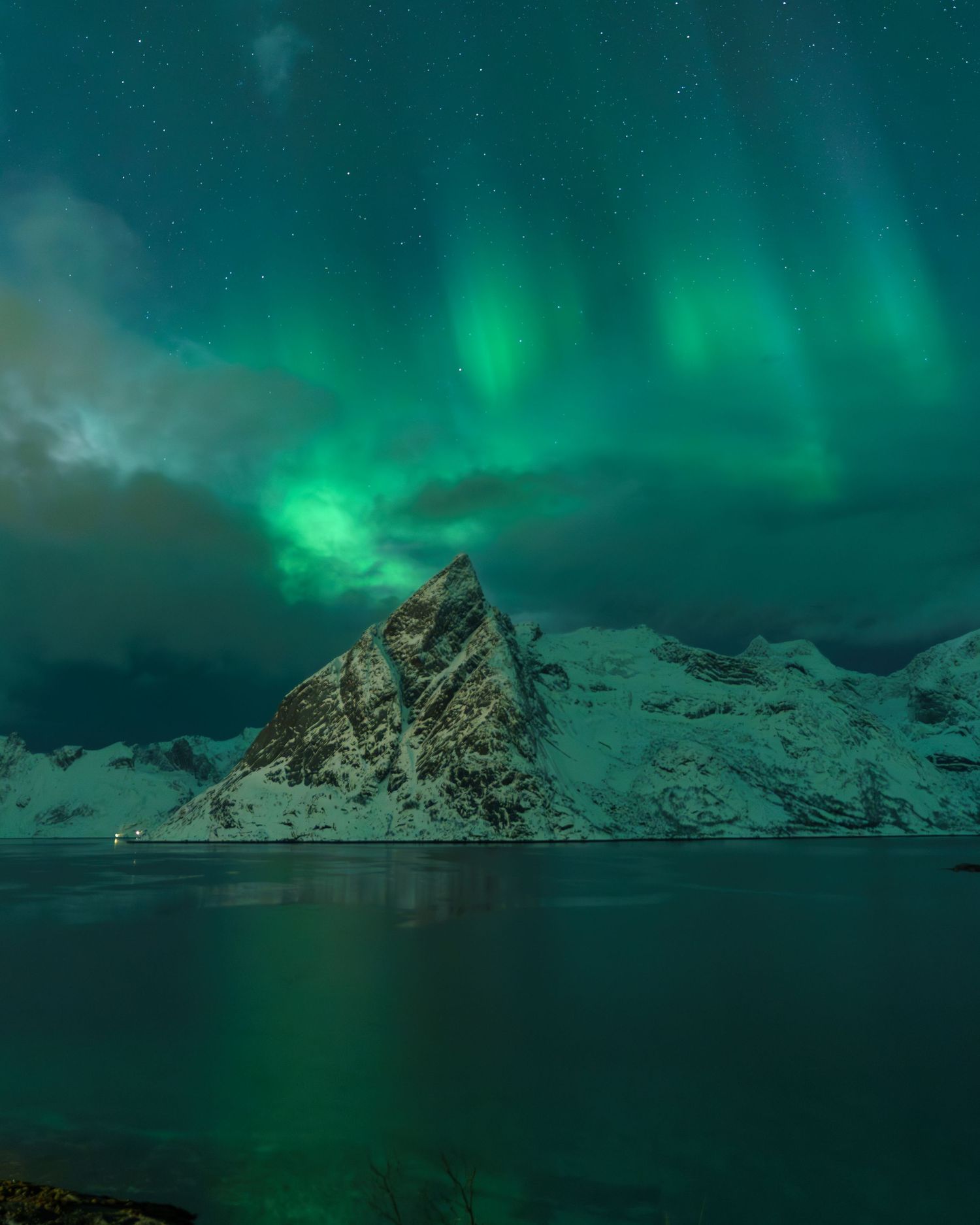 Black sand beach with golden grass, dramatic mountain peaks shrouded in clouds, Iceland's Vestrahorn landscape.