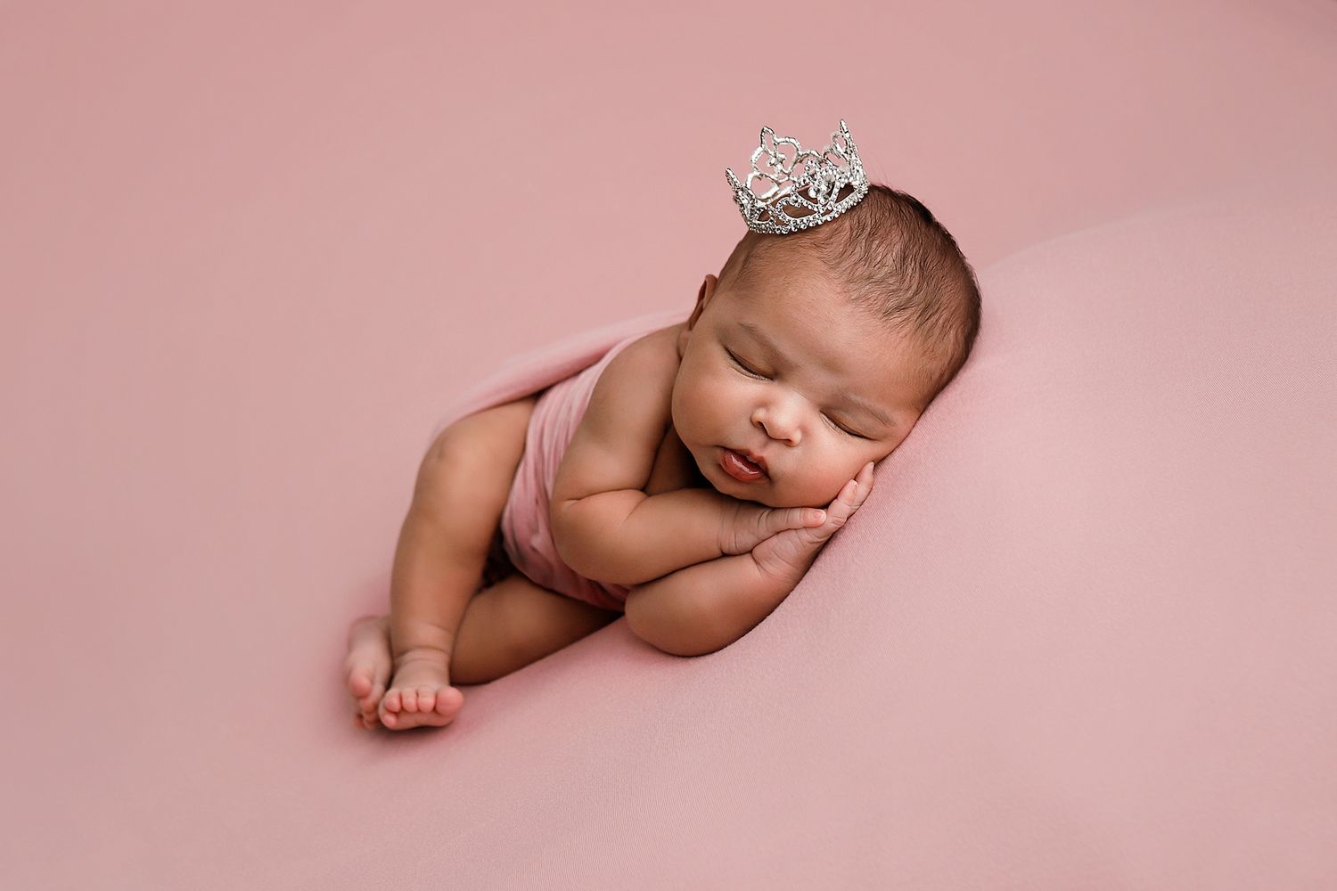 Sleeping newborn baby wearing a silver crown on a pink background. Utah County newborn photographer