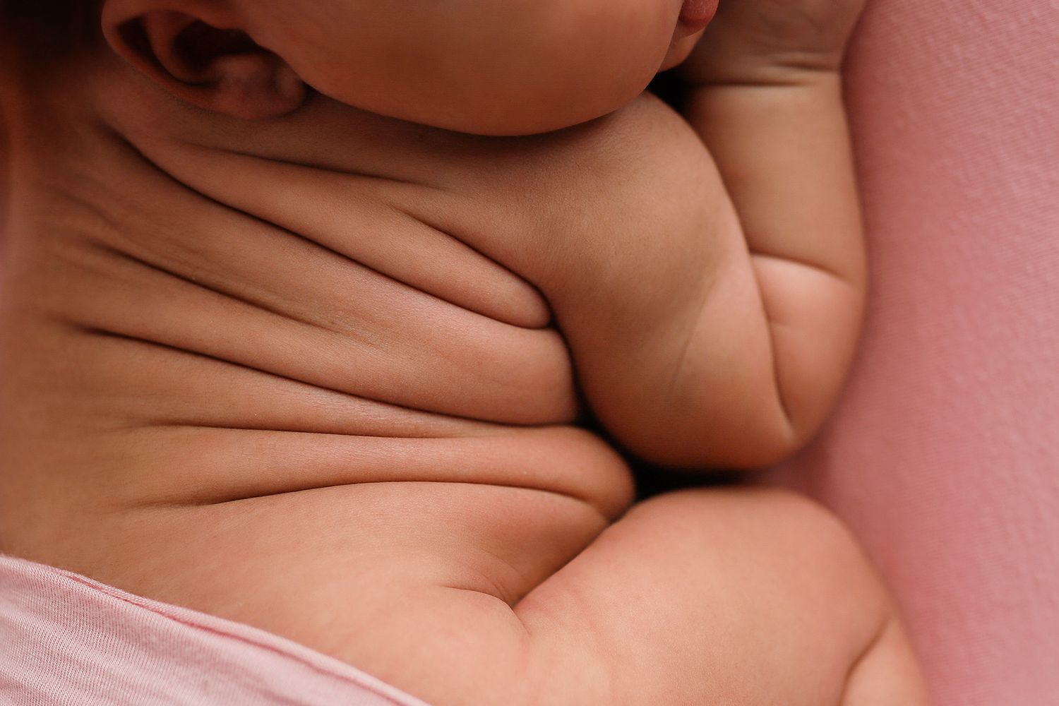 Close-up of chubby newborn baby neck rolls and skin folds, showcasing healthy infant weight on pink background.