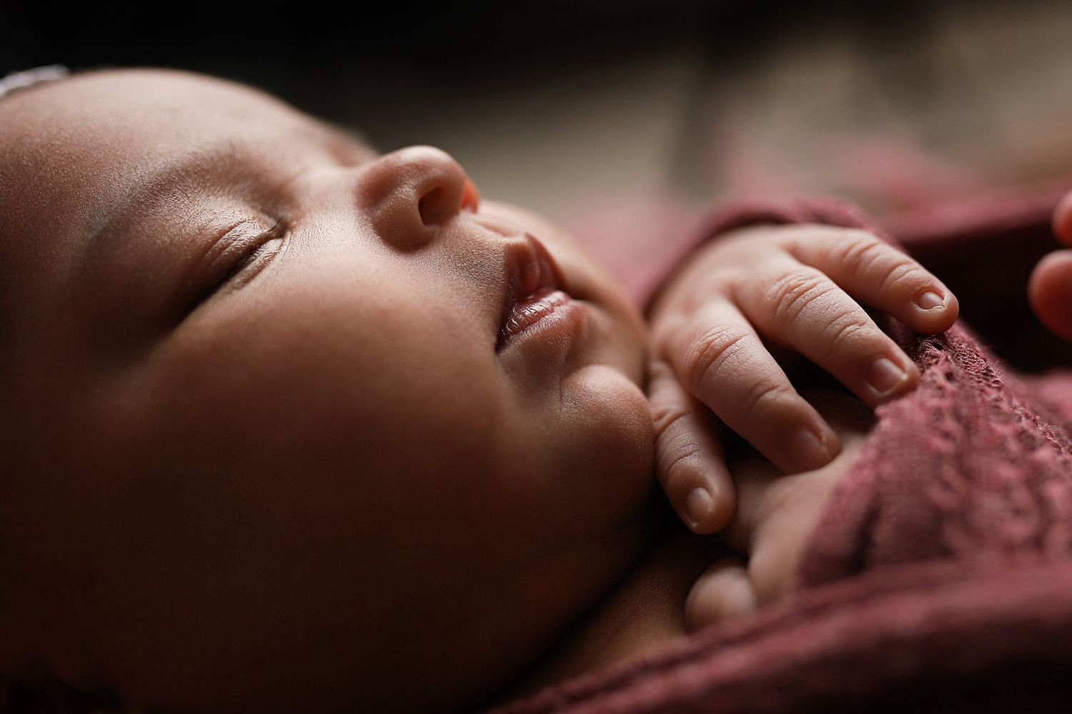 Peaceful newborn baby sleeping wrapped in a soft pink blanket with tiny hands resting near face.