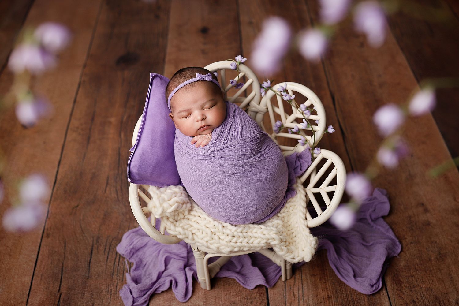 Newborn baby girl swaddled in purple wrap sleeping in a white bicycle prop on a wooden floor. Utah County newborn photographer