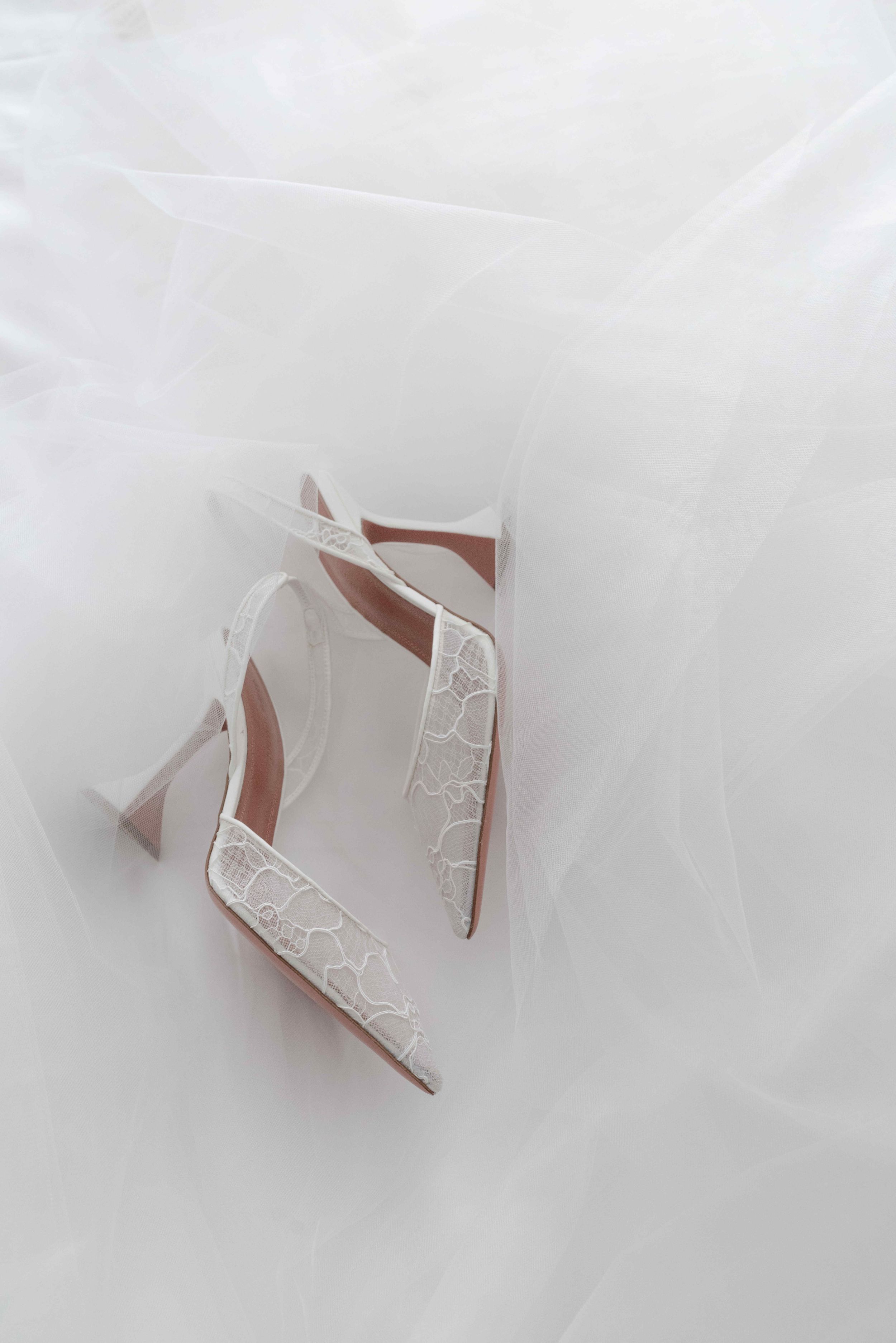 Elegant white lace bridal heels with slingback design resting on soft tulle wedding dress fabric.