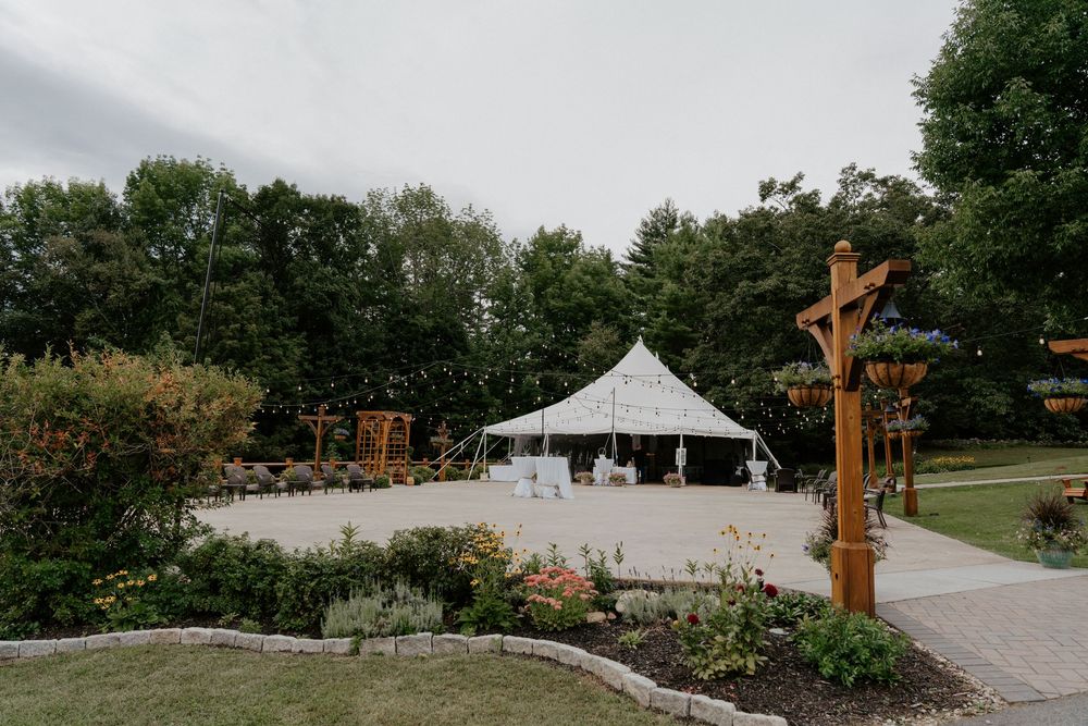Elegant white tent pavilion surrounded by lush gardens and trees at an outdoor wedding venue.