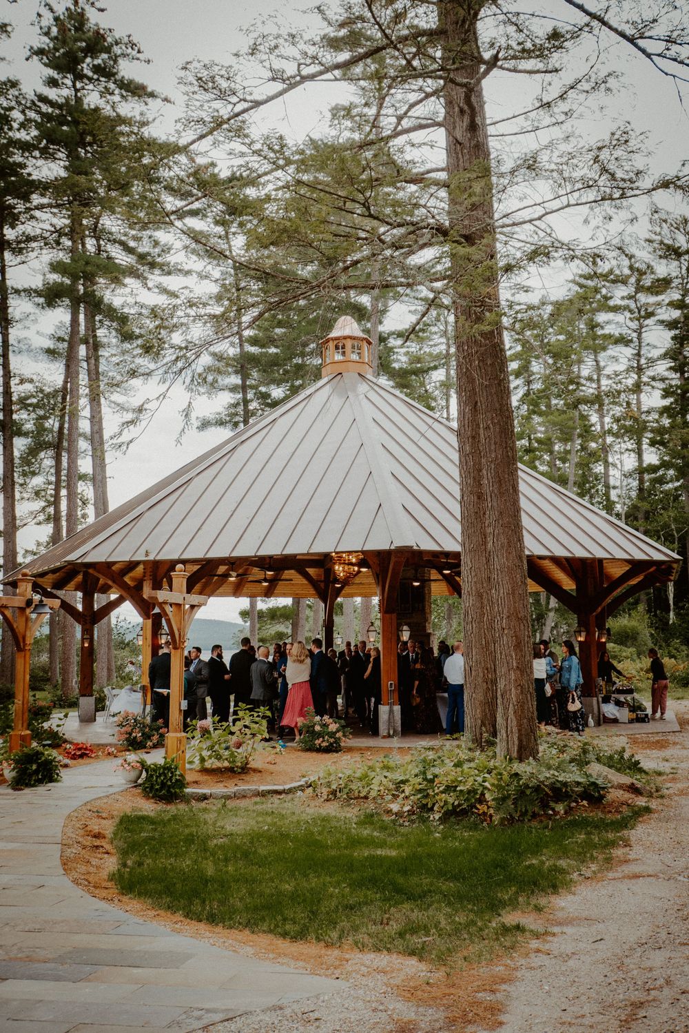 Rustic wooden gazebo wedding ceremony venue nestled among tall pine trees with guests gathered inside.