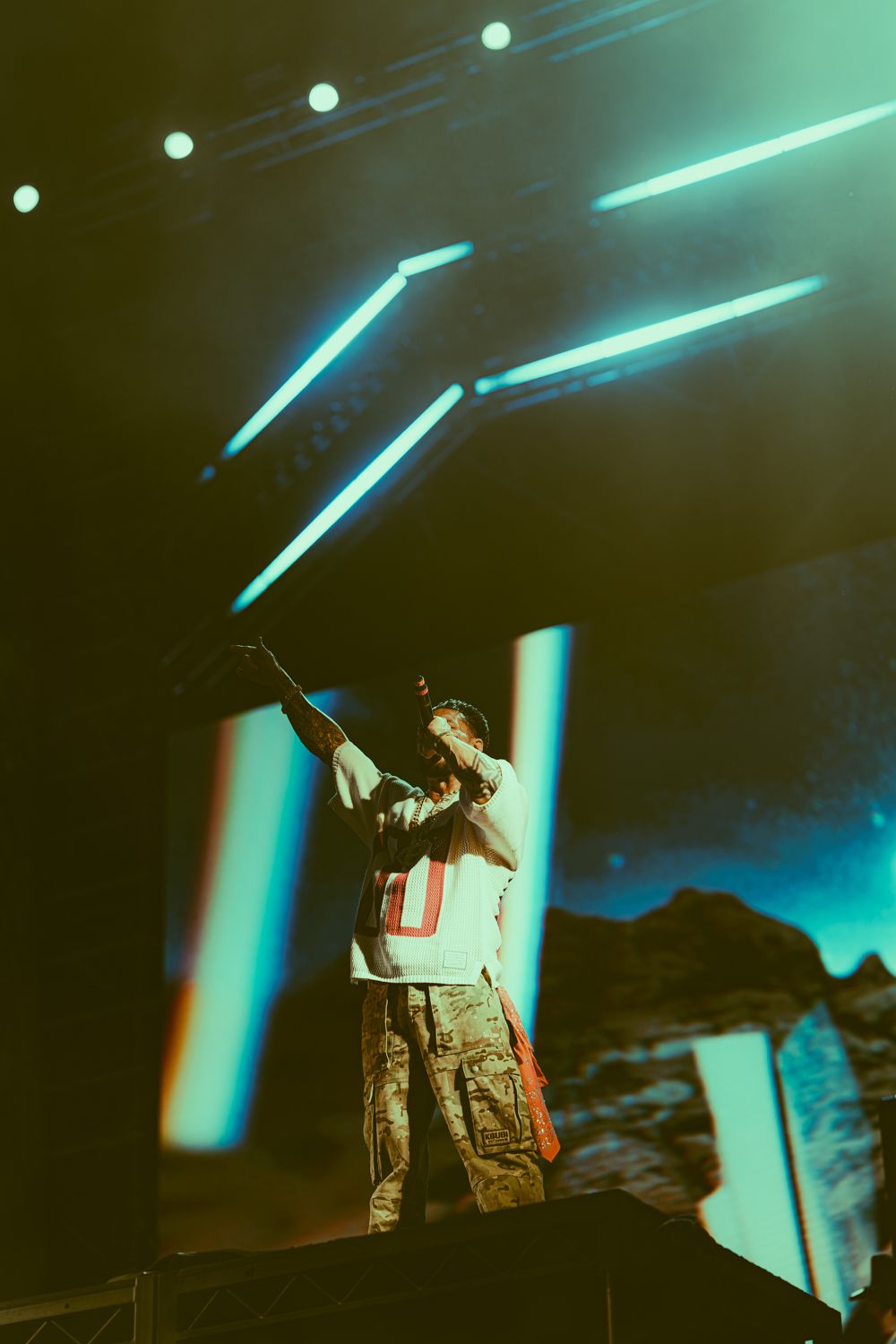 Performer on stage with teal neon lights and dramatic backdrop at a live concert event.