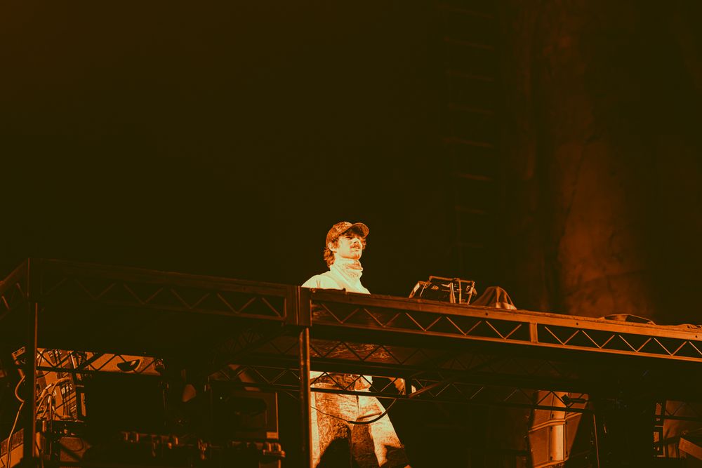 Performer stands on stage under dramatic warm lighting during a live concert event.