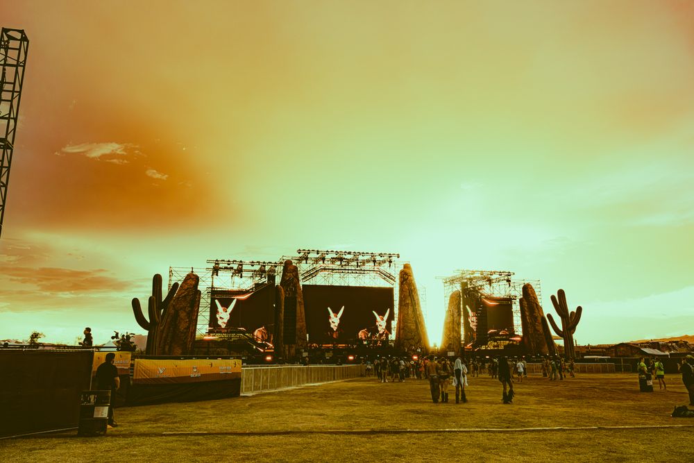 Outdoor music festival stage with cactus decorations under a dramatic golden sunset sky.