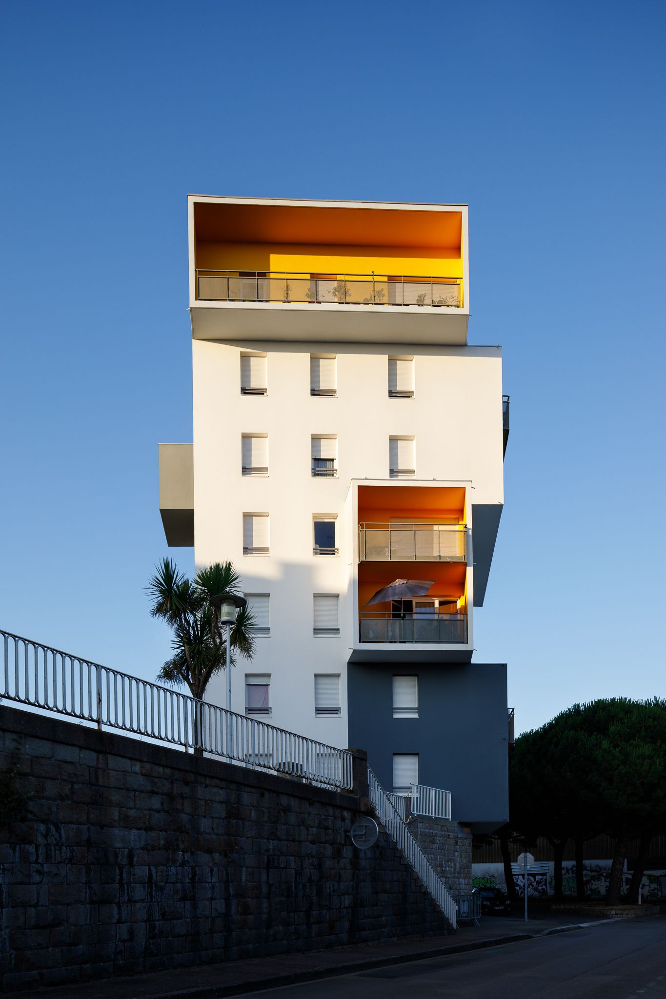 Immeuble résidentiel moderne à plusieurs étages, doté de balcons aux couleurs jaune et orange audacieuses, se détachant sur un ciel bleu