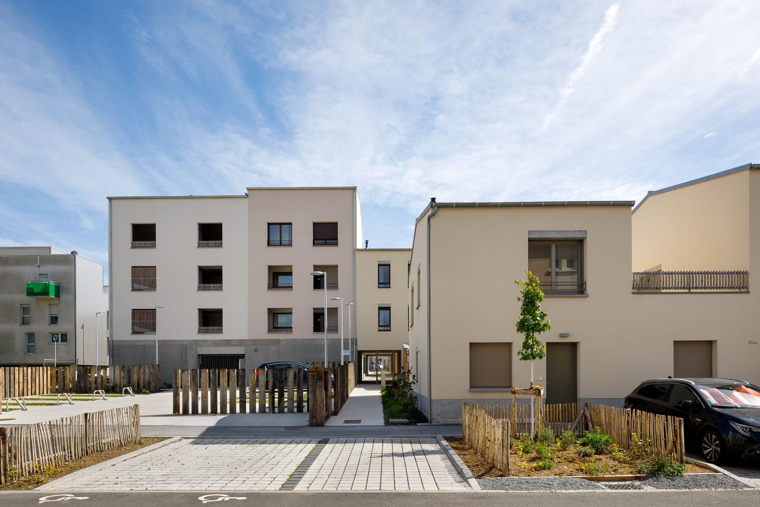 Nouveau complexe résidentiel composé de bâtiments cubiques beiges et blancs, avec des clôtures en bois et une cour pavée