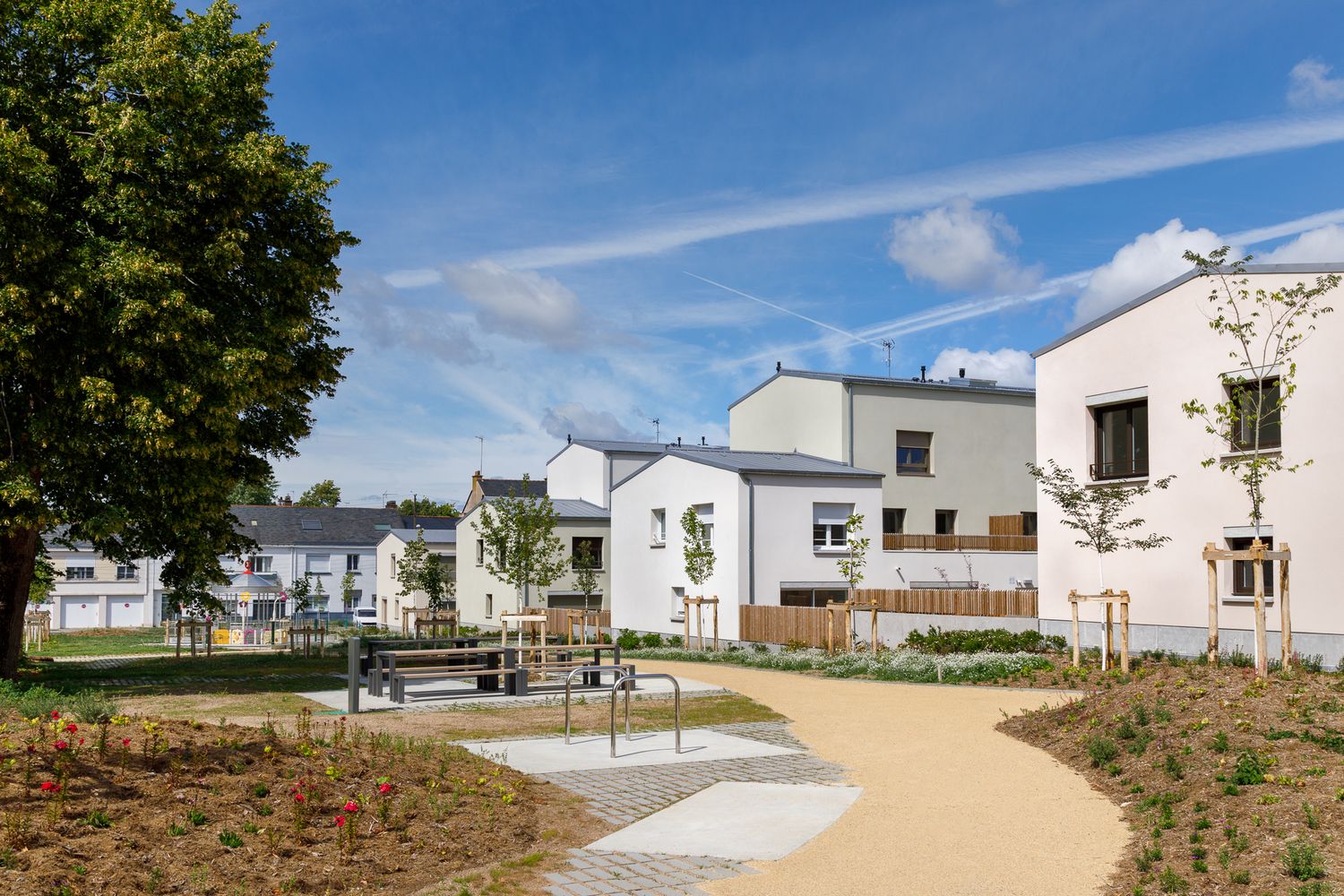 Ensemble résidentiel composé de bâtiments blancs entourant un jardin commun paysager, agrémenté d'allées et d'espaces de détentes