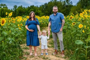 Pregnant woman in blue dress with husband and toddler posing in sunflower field for maternity photo.
