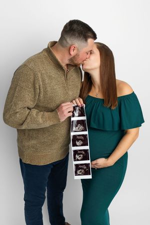 Couple kissing while holding ultrasound photos, pregnant woman in green dress cradling baby bump, pregnancy announcement.