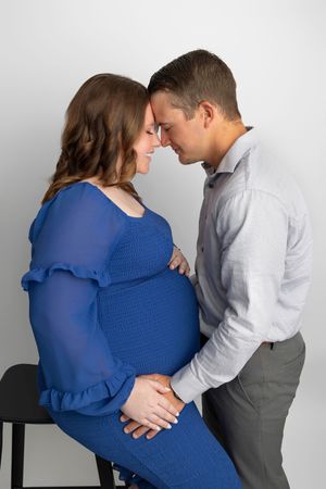 Couple sharing a tender forehead-to-forehead moment, pregnant woman in blue dress with partner in gray shirt.