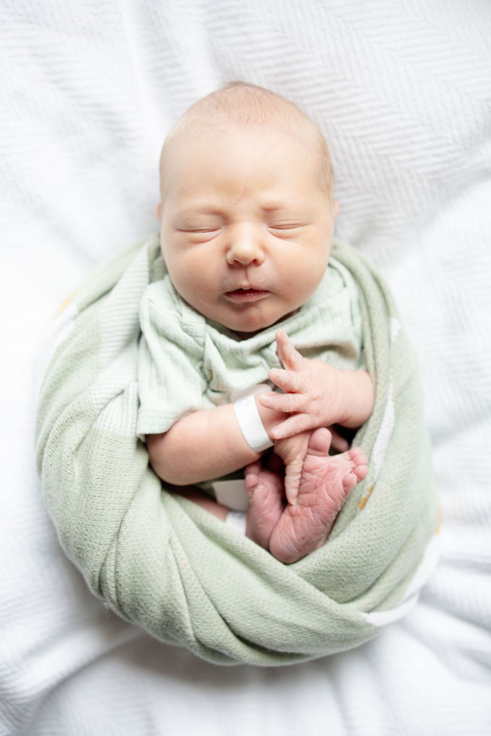 Peaceful newborn baby swaddled in a soft green wrap during fresh 48 session at the University of Tennessee with Nina Thomas Photography.