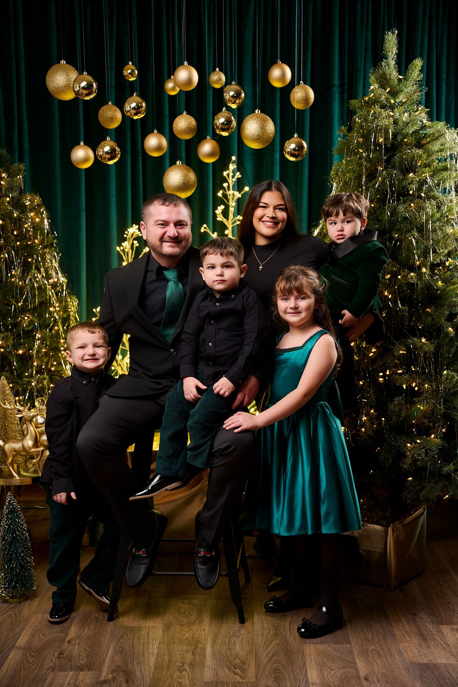 Family of six posing for a festive Christmas portrait with gold ornaments and green velvet backdrop.