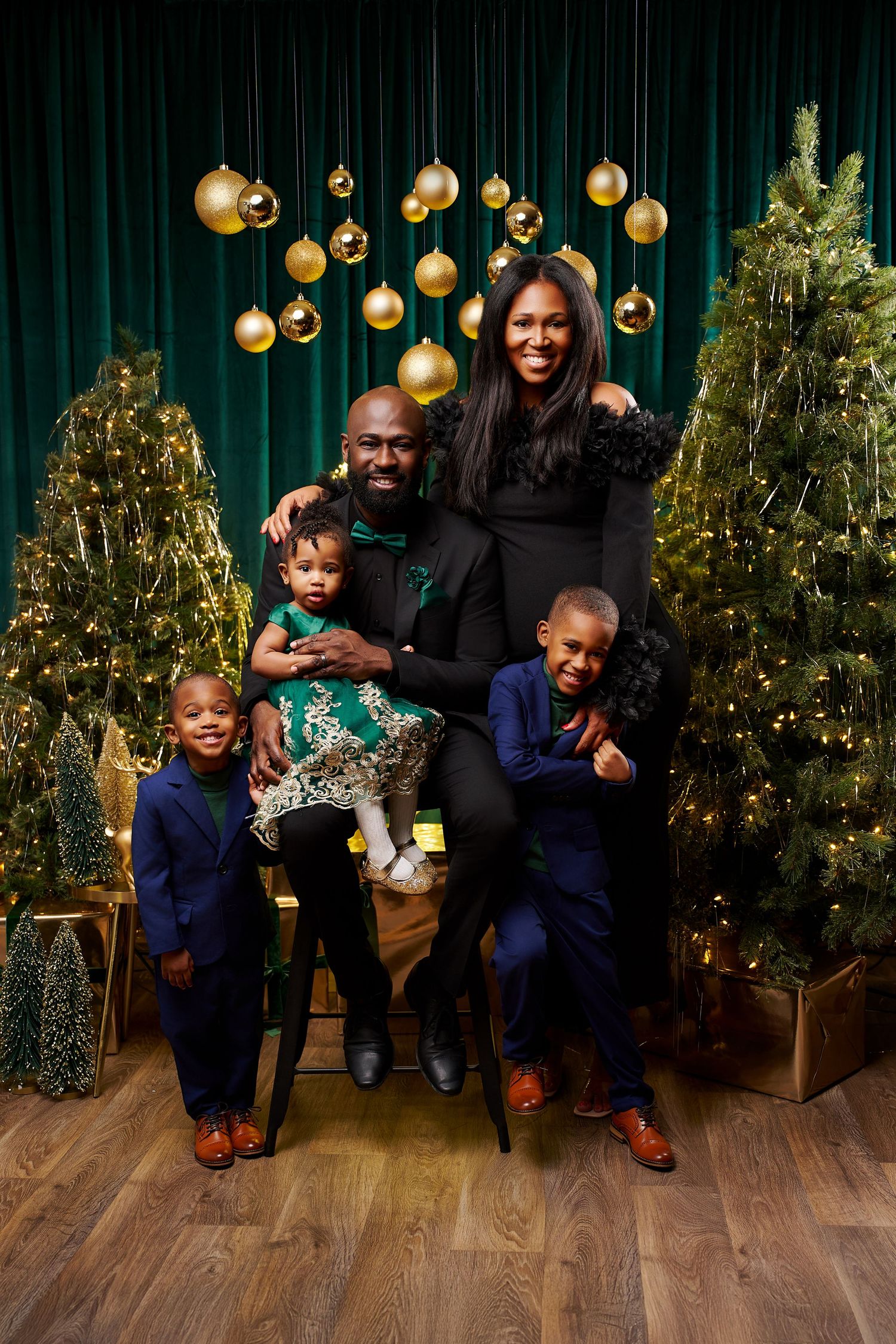 Happy family of five posing together in elegant attire among Christmas trees with gold ornaments.