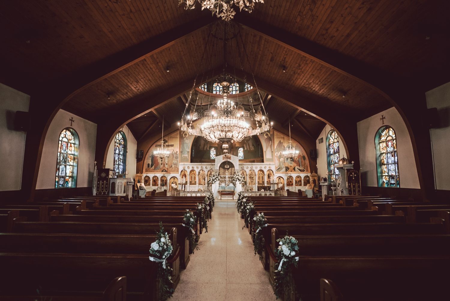 Elegant church interior with wooden pews, stained glass windows, and chandeliers set for a wedding ceremony.