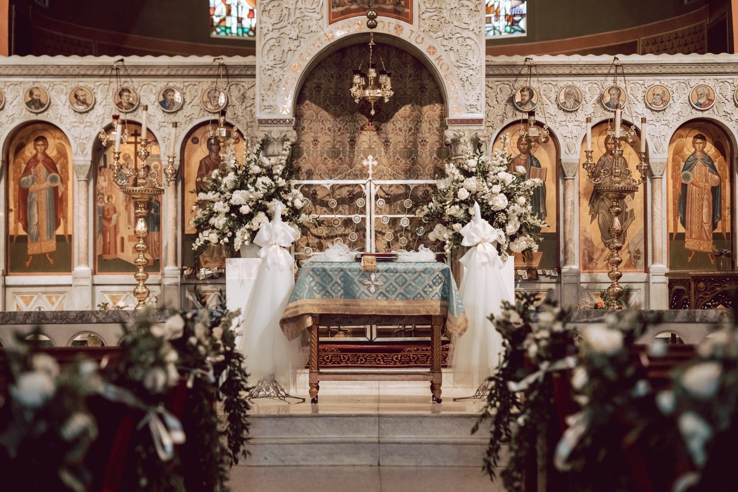 Elegant Orthodox church altar adorned with white floral arrangements and greenery for a wedding ceremony.