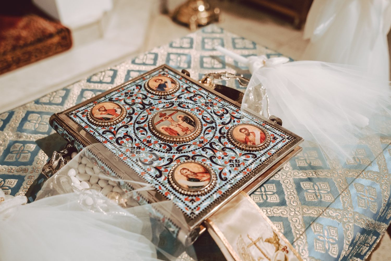 Ornate Orthodox Bible with intricate enamel cover featuring religious icons, displayed on decorative stand at a wedding ceremony.