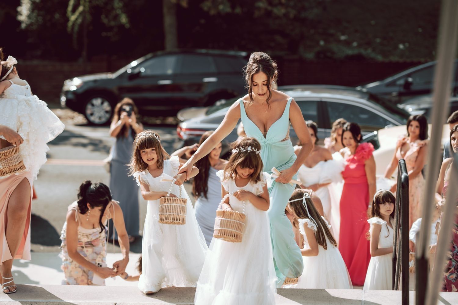 Bridesmaid in blue dress guides flower girls with baskets down wedding aisle.