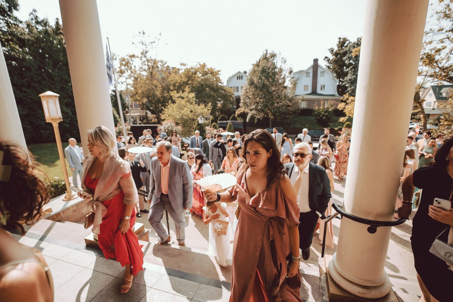 Wedding guests descending outdoor steps at an elegant venue surrounded by white columns and lush greenery.