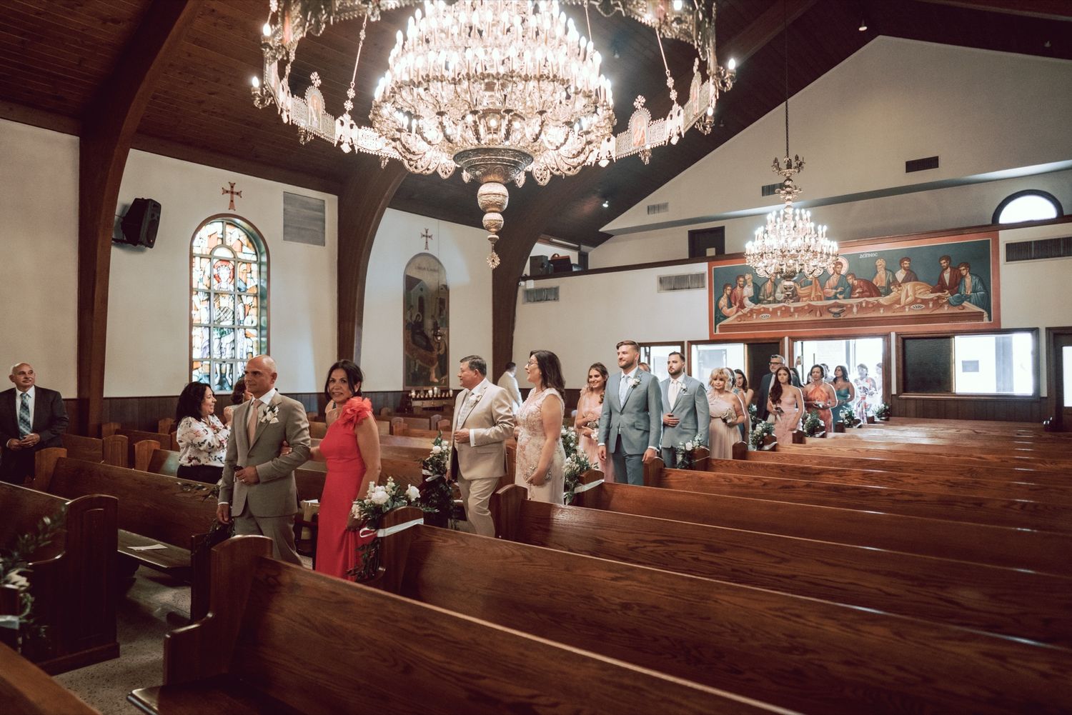 Wedding party and guests gathered in an elegant church with crystal chandeliers during a ceremony.