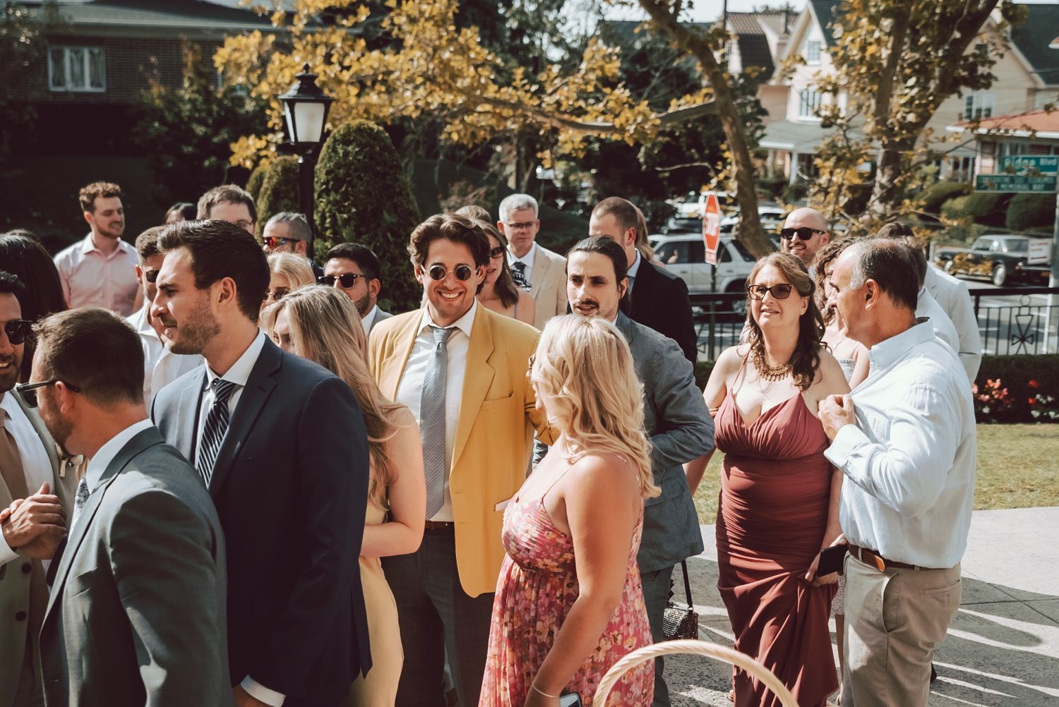 Smiling wedding guests in formal attire, featuring a man in a yellow blazer, gathered outdoors.
